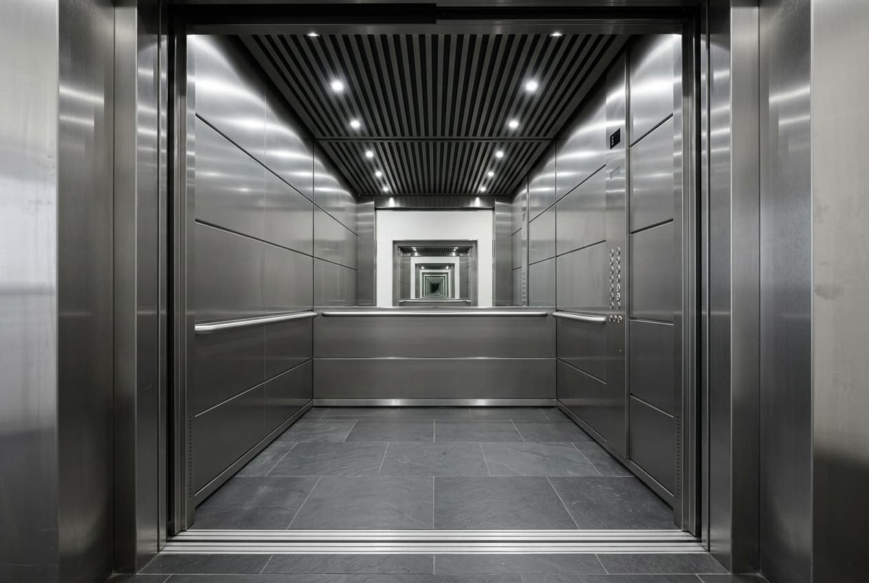The interior of an empty lift car, brushed metal walls and a handrail.